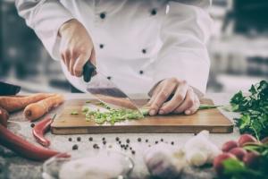 Chef chopping up carrots and scallions on a cutting board