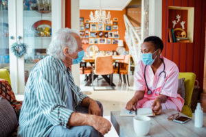 elderly man with a mask talking to his private caregiver in a mask in the living room